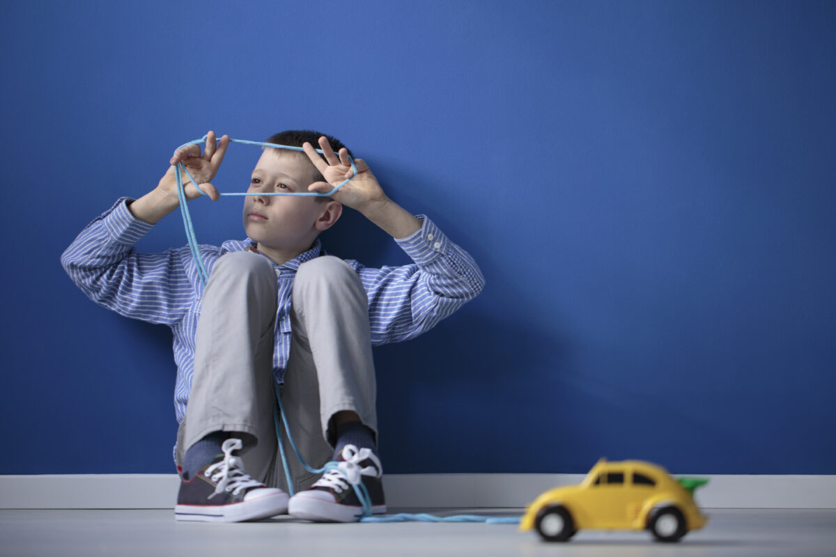 Autistic child playing with a string and a yellow toy car against a blue wall with copy space