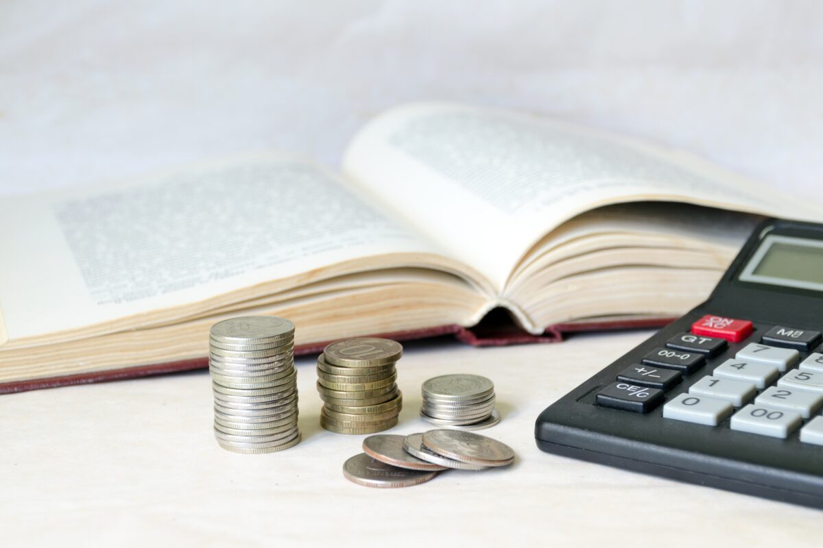 A stack of coins and a calculator in front of an open book. The concept of expensive education and low scholarship